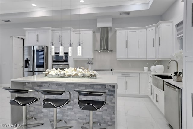 kitchen featuring stainless steel appliances, wall chimney range hood, a sink, and white cabinetry