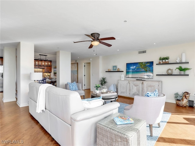 living room with light wood-type flooring, visible vents, ceiling fan, and baseboards