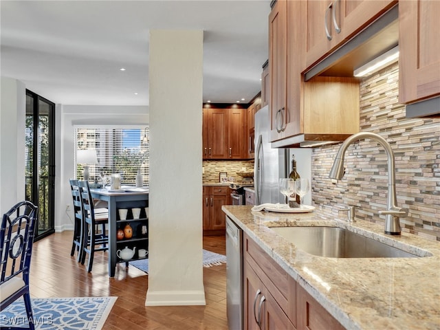 kitchen with appliances with stainless steel finishes, light stone counters, wood finished floors, a sink, and backsplash