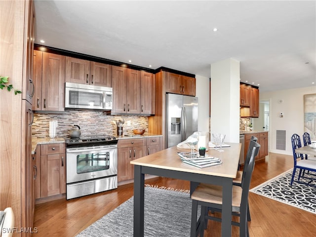 kitchen with brown cabinets, stainless steel appliances, light countertops, visible vents, and wood finished floors