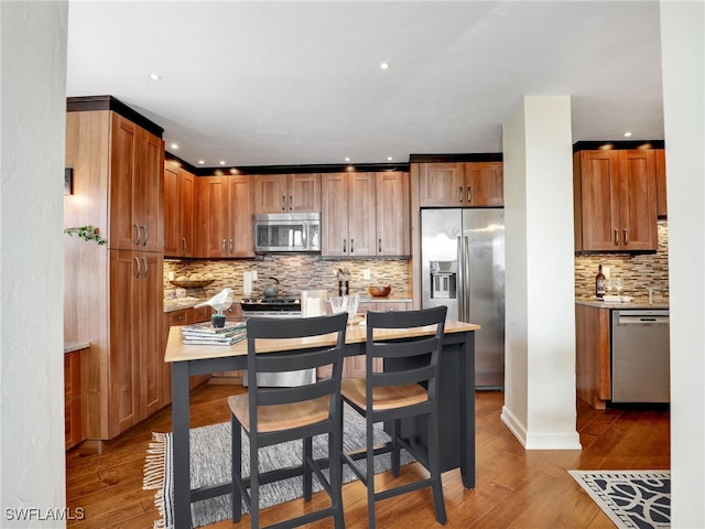 kitchen with light wood finished floors, appliances with stainless steel finishes, brown cabinetry, and light countertops