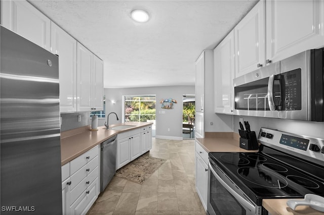 kitchen with appliances with stainless steel finishes, sink, white cabinets, and a textured ceiling