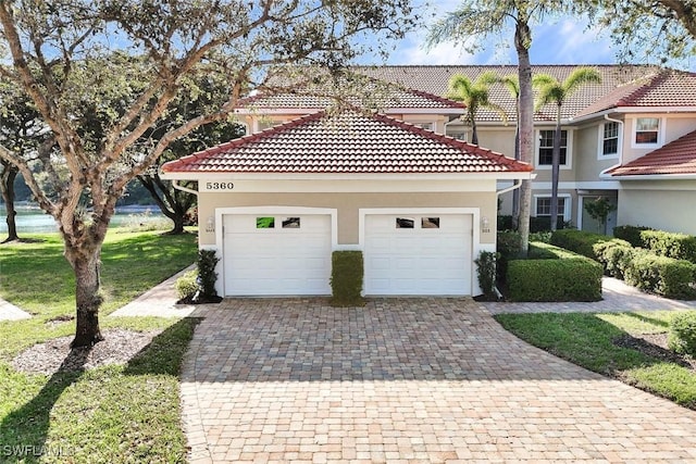 mediterranean / spanish home with a garage, a front yard, decorative driveway, and stucco siding