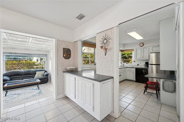 kitchen featuring stainless steel fridge, black dishwasher, light tile patterned floors, and white cabinets