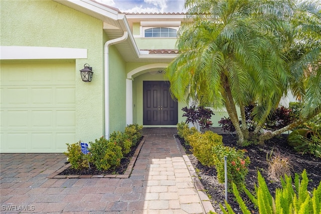 entrance to property with a garage and stucco siding