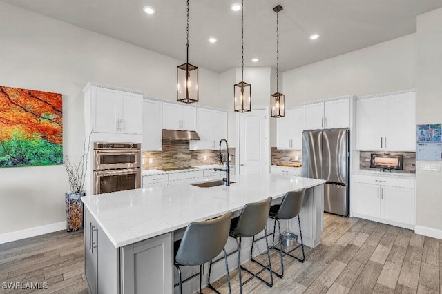 kitchen featuring a kitchen island with sink, sink, stainless steel appliances, and white cabinets