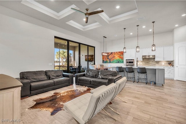 living room with a towering ceiling, coffered ceiling, ceiling fan, light hardwood / wood-style floors, and crown molding