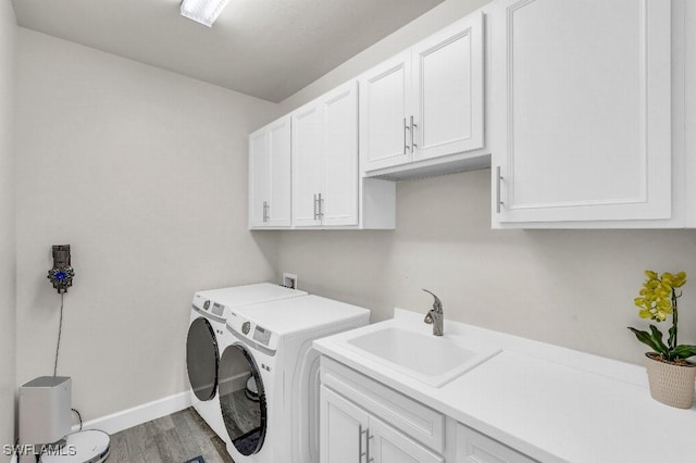 clothes washing area featuring cabinets, wood-type flooring, sink, and washing machine and clothes dryer