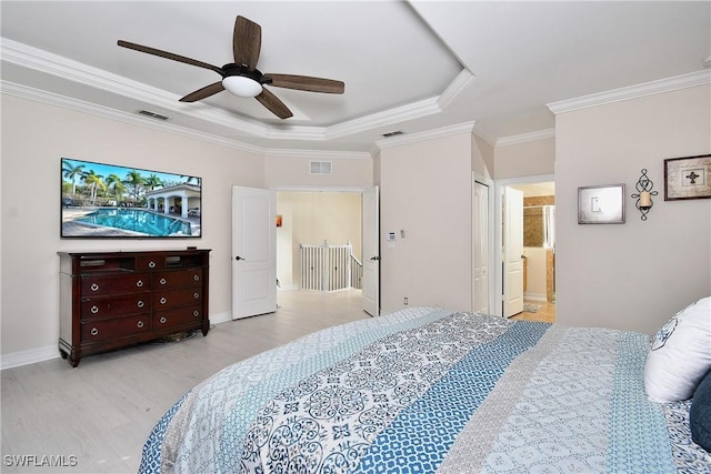 bedroom featuring ensuite bath, ornamental molding, a tray ceiling, and light wood-type flooring