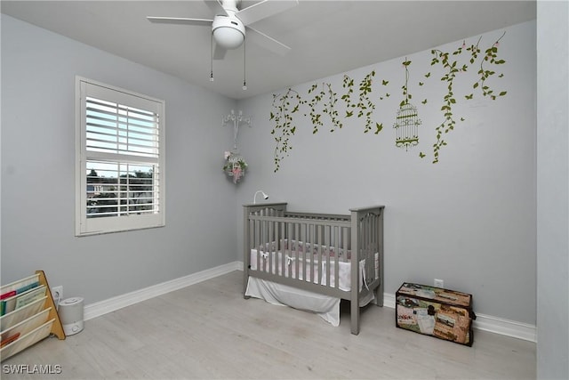 bedroom featuring light hardwood / wood-style flooring, a crib, and ceiling fan