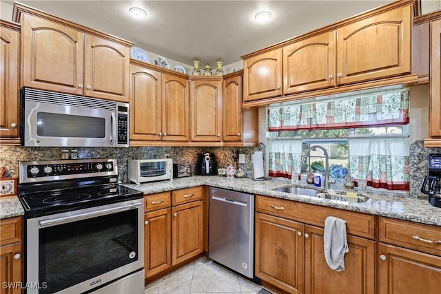 kitchen featuring stainless steel appliances, sink, backsplash, and light stone counters