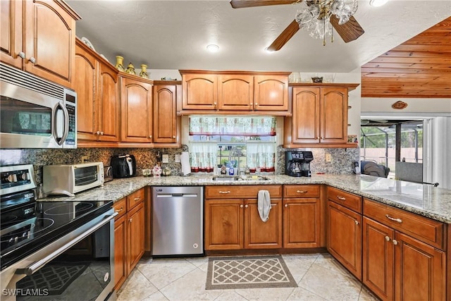 kitchen featuring sink, ceiling fan, appliances with stainless steel finishes, light stone counters, and decorative backsplash