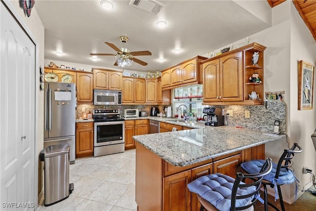 kitchen featuring sink, decorative backsplash, light stone counters, kitchen peninsula, and stainless steel appliances