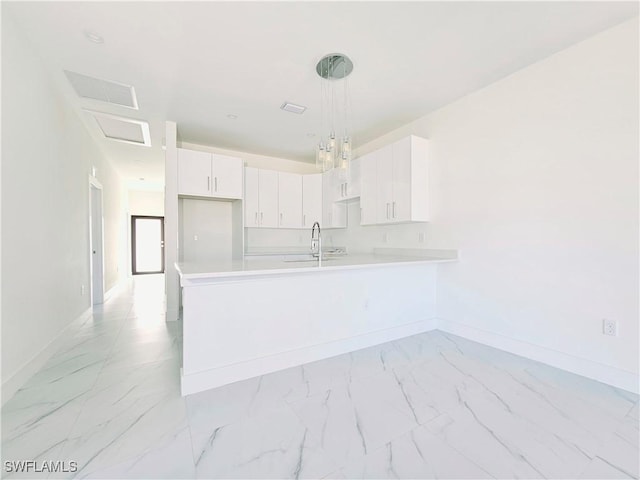 kitchen with marble finish floor, light countertops, hanging light fixtures, white cabinetry, and a peninsula