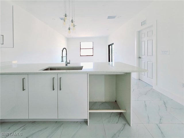 kitchen featuring a sink, white cabinets, marble finish floor, hanging light fixtures, and light countertops