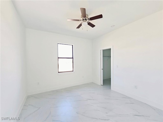 empty room with a ceiling fan, marble finish floor, and baseboards