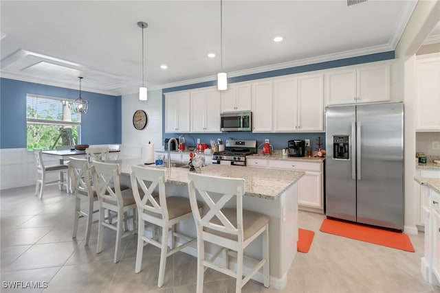 kitchen with appliances with stainless steel finishes, light stone counters, decorative light fixtures, white cabinets, and an island with sink