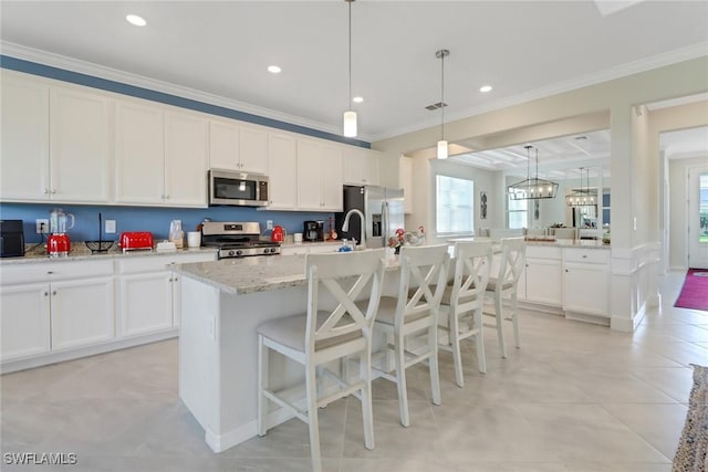 kitchen featuring white cabinets, appliances with stainless steel finishes, pendant lighting, and a kitchen island with sink