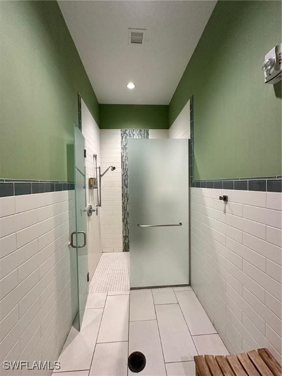 bathroom with tile patterned flooring, a shower with door, and tile walls