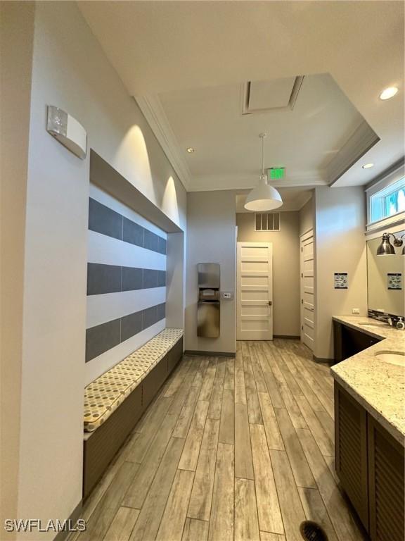 kitchen featuring sink, crown molding, light stone counters, pendant lighting, and light hardwood / wood-style floors