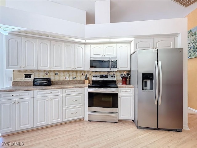 kitchen with tasteful backsplash, appliances with stainless steel finishes, white cabinets, and light wood-type flooring