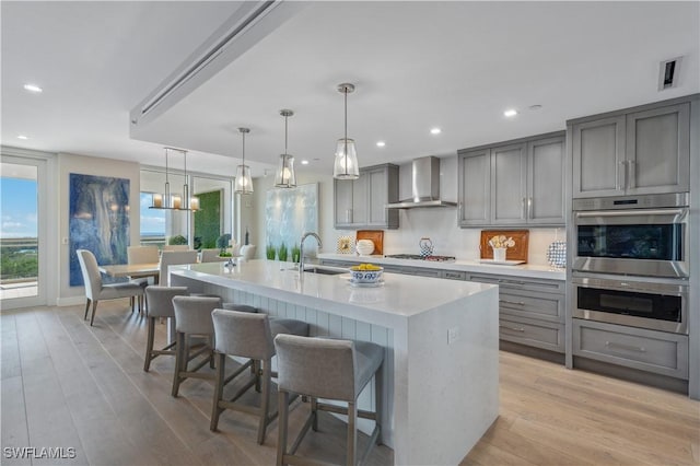 kitchen featuring a large island, wall chimney range hood, sink, a breakfast bar, and appliances with stainless steel finishes