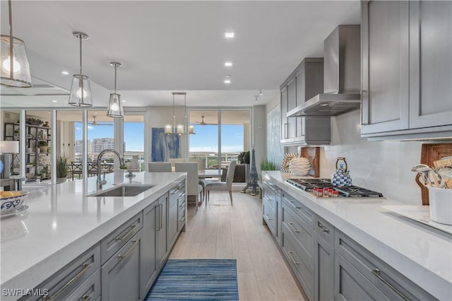 kitchen with sink, decorative light fixtures, gray cabinets, and wall chimney exhaust hood