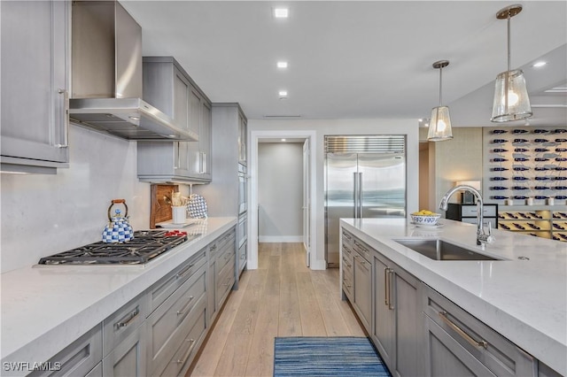 kitchen with wall chimney range hood, sink, appliances with stainless steel finishes, gray cabinetry, and hanging light fixtures