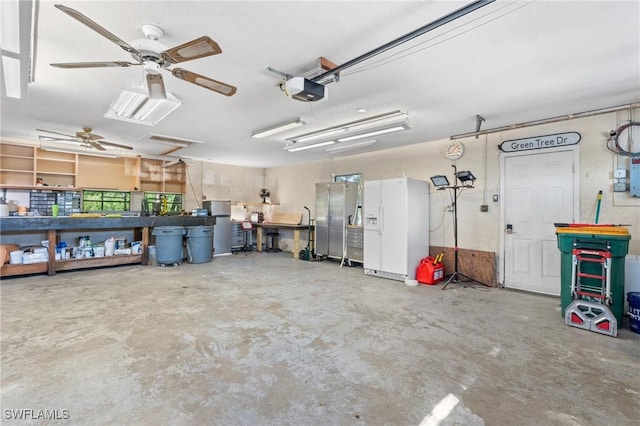 garage featuring a garage door opener, white refrigerator with ice dispenser, ceiling fan, and a workshop area