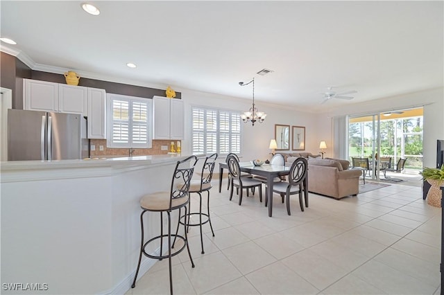 kitchen featuring stainless steel fridge, white cabinetry, tasteful backsplash, ornamental molding, and a kitchen bar