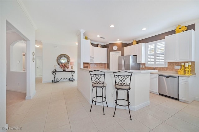 kitchen with light tile patterned flooring, crown molding, appliances with stainless steel finishes, a kitchen breakfast bar, and white cabinets