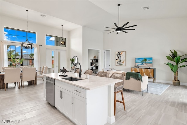 kitchen with sink, white cabinetry, light stone counters, decorative light fixtures, and a kitchen island with sink