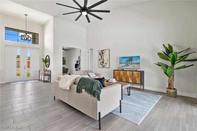 living room featuring ceiling fan with notable chandelier, french doors, and a high ceiling