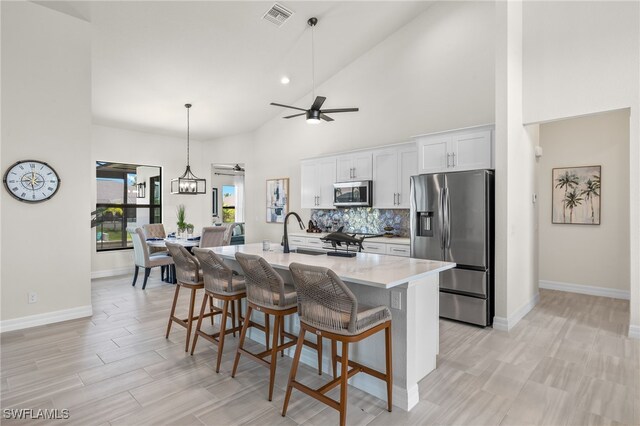 kitchen with white cabinetry, backsplash, stainless steel appliances, an island with sink, and a kitchen bar