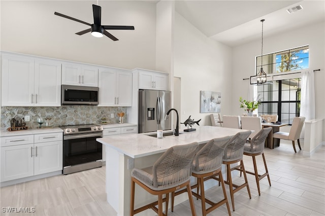 kitchen featuring white cabinetry, a kitchen island with sink, a kitchen breakfast bar, and appliances with stainless steel finishes