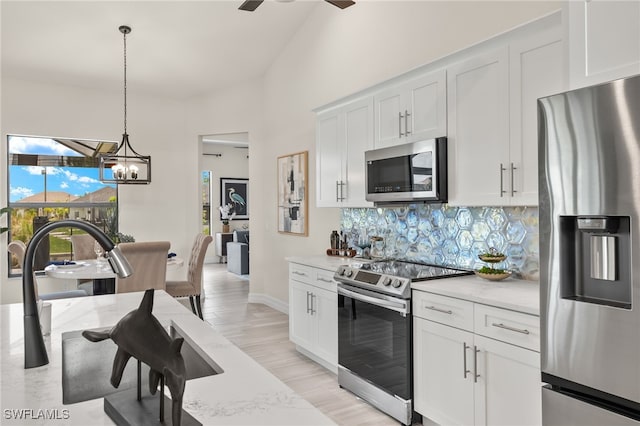 kitchen with stainless steel appliances, decorative light fixtures, light stone countertops, and white cabinets