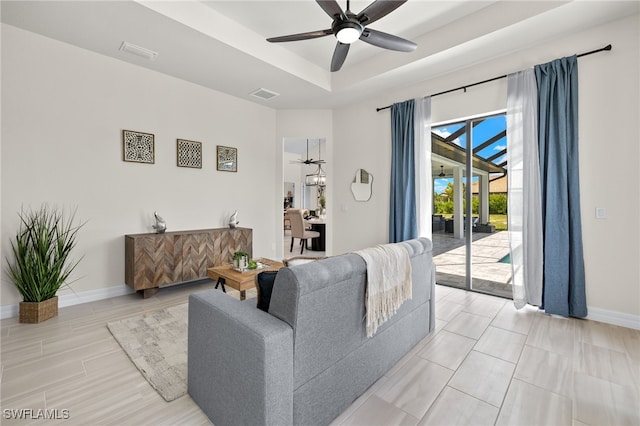 living room featuring ceiling fan, a raised ceiling, and light wood-type flooring