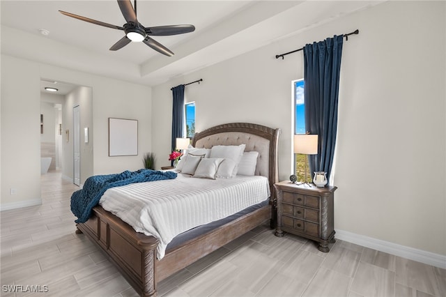 bedroom with a raised ceiling, ceiling fan, and ensuite bath