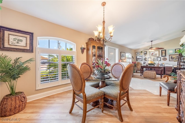 dining space with ceiling fan with notable chandelier, vaulted ceiling, and light hardwood / wood-style flooring