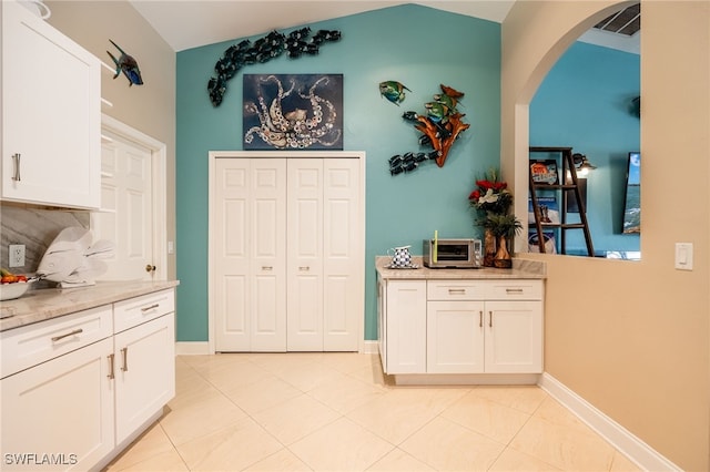 kitchen featuring vaulted ceiling, white cabinets, backsplash, light tile patterned floors, and light stone countertops