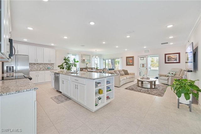 kitchen featuring appliances with stainless steel finishes, white cabinetry, backsplash, light stone counters, and an island with sink