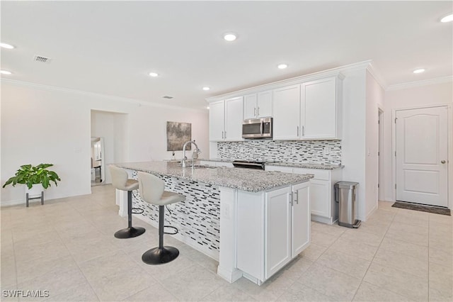 kitchen featuring sink, white cabinetry, a center island with sink, stainless steel appliances, and light stone countertops