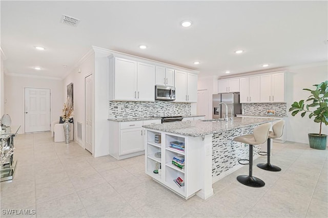 kitchen with white cabinetry, stainless steel appliances, light stone countertops, ornamental molding, and a center island with sink