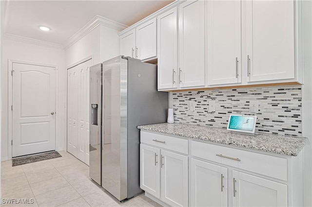 kitchen with white cabinetry, crown molding, light tile patterned floors, stainless steel fridge, and backsplash