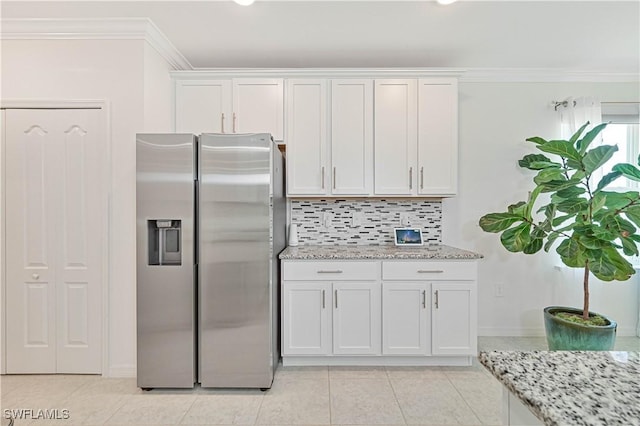 kitchen with crown molding, stainless steel fridge, backsplash, light stone counters, and white cabinets