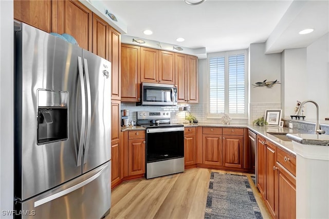 kitchen with appliances with stainless steel finishes, sink, decorative backsplash, kitchen peninsula, and light hardwood / wood-style flooring