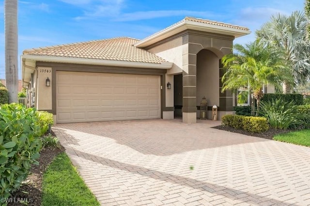 mediterranean / spanish home with a garage, a tile roof, decorative driveway, and stucco siding