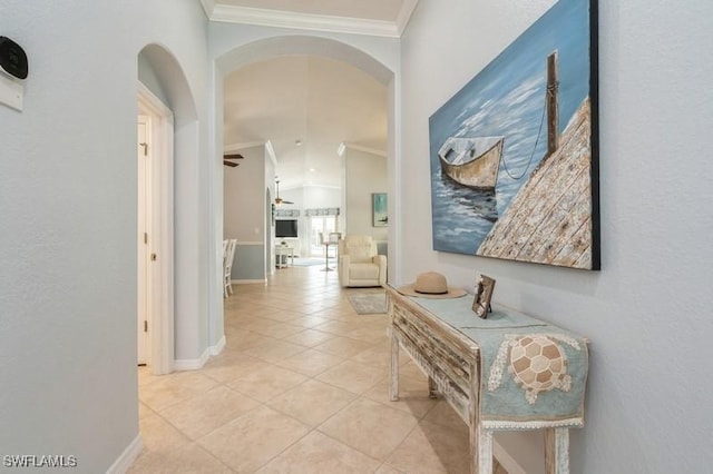 corridor featuring arched walkways, crown molding, light tile patterned floors, vaulted ceiling, and baseboards