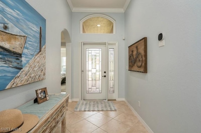 foyer featuring light tile patterned floors, ornamental molding, arched walkways, and baseboards