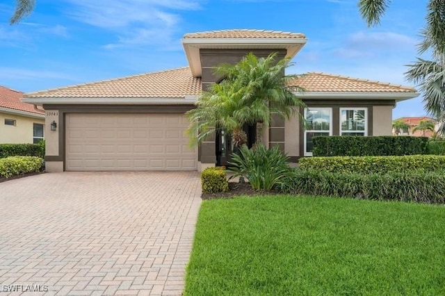 view of front of house featuring an attached garage, a tile roof, decorative driveway, stucco siding, and a front lawn